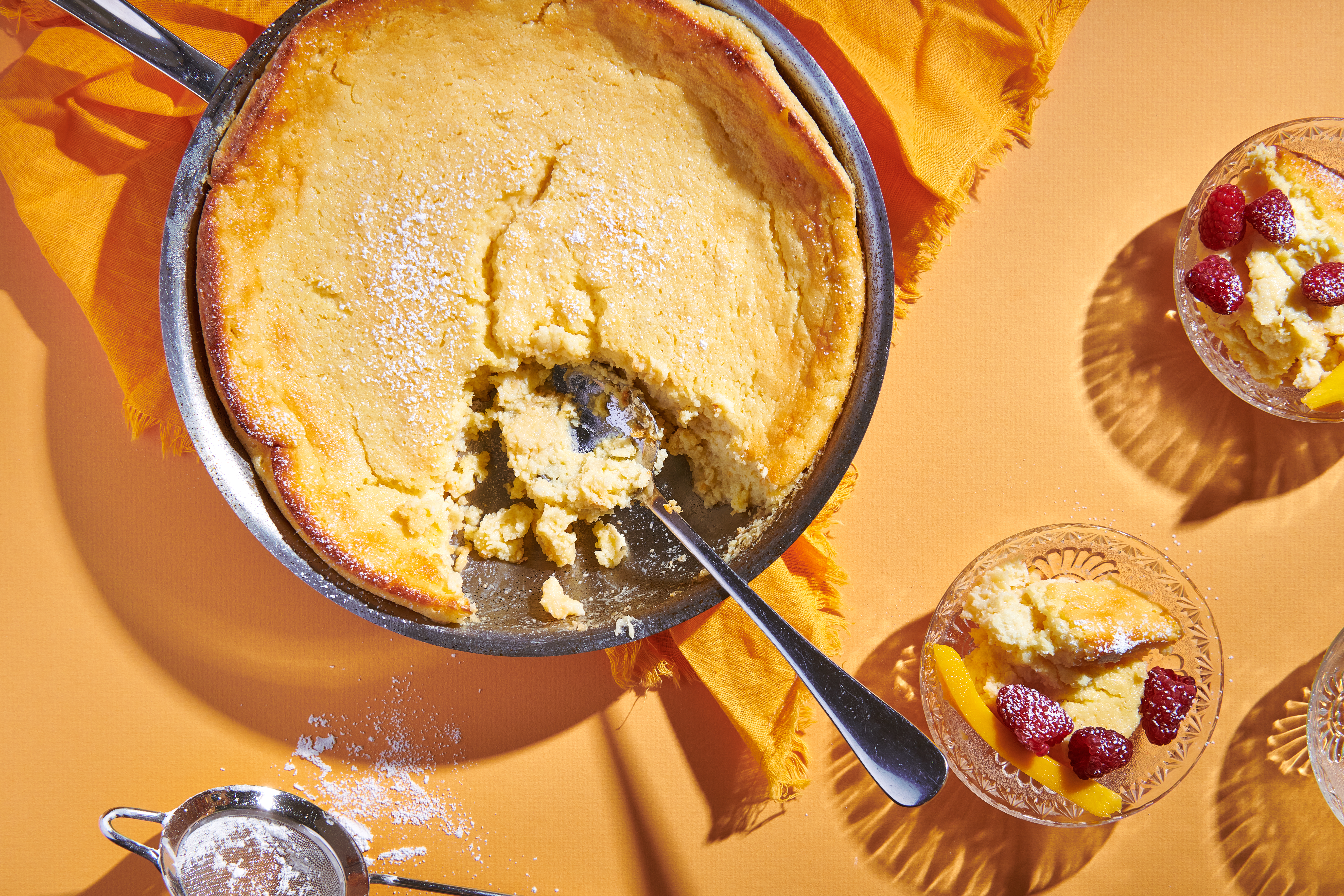 Mango pudding cake served in the skillet alongside two bowls of cake garnished with fresh berries.