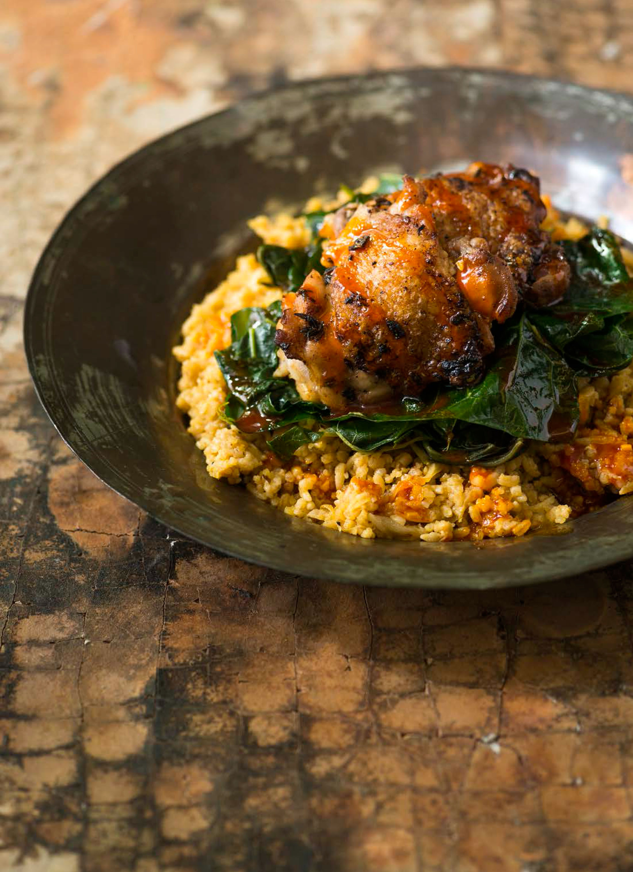 A bowl of chicken thighs atop sauteed greens and rice.