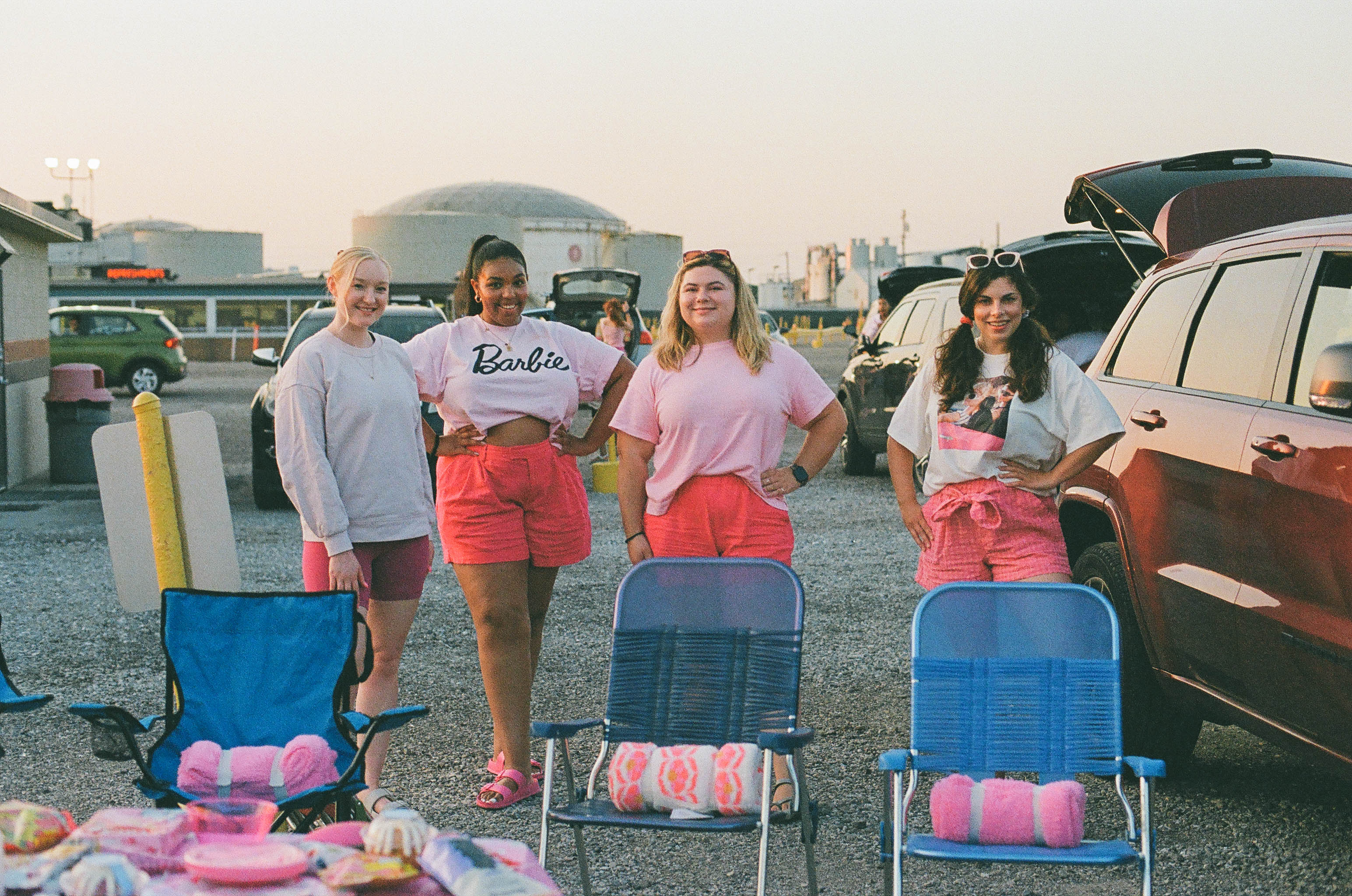 Four women standing behind chairs in a drive-in movie theater parking lot