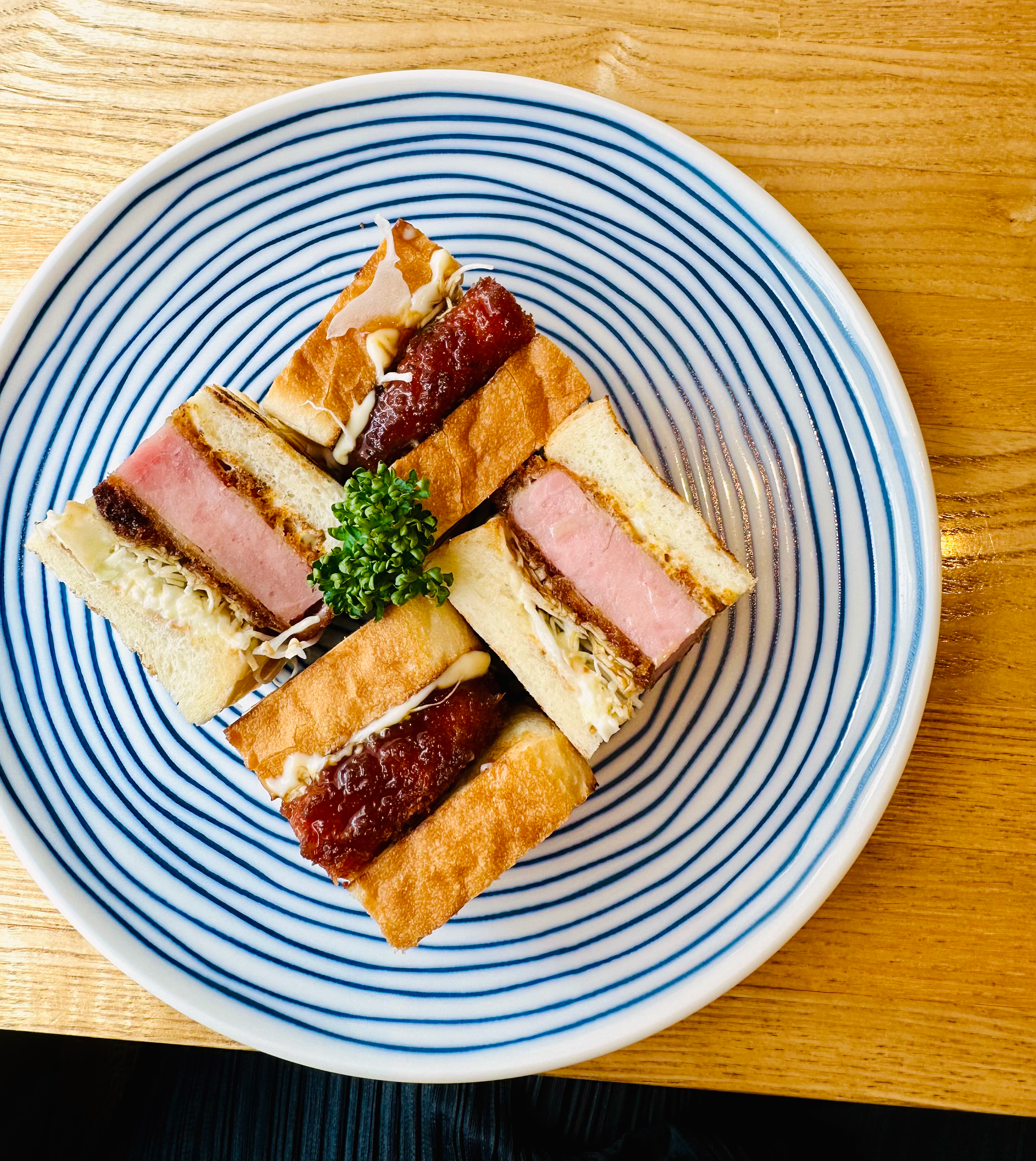 A meaty katsu sandwich cut into four sections, presented side-up on a plate decorated with blue spirals.