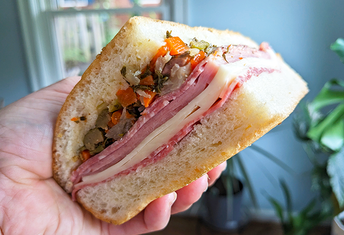 The writer holds a muffuletta, packed with deli meats, olives, and more.